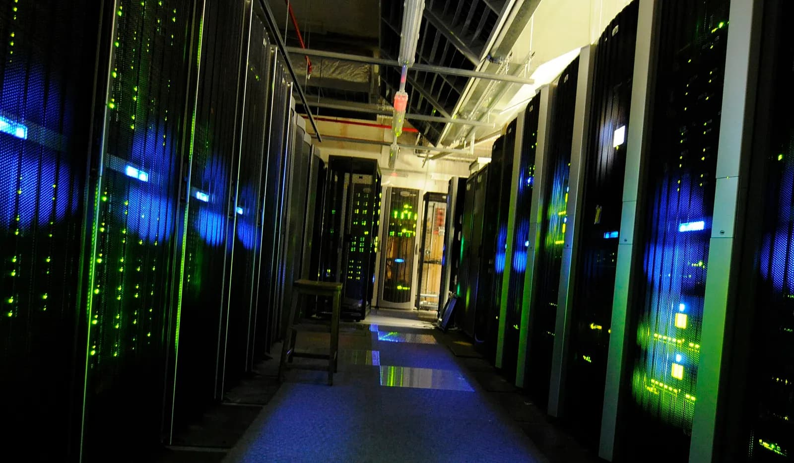 Aisle of a dark server room, racks lit by green and blue status lights