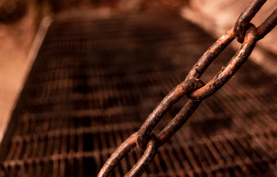 Close-up of a rusty chain above a metal grate