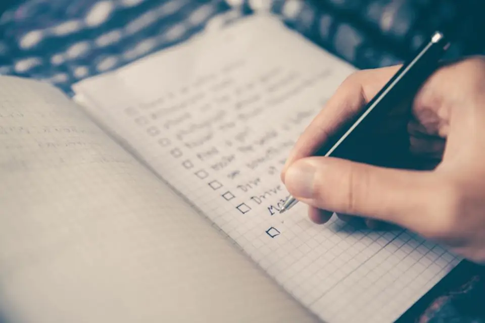 A hand ticking a to-do list in a grid notebook