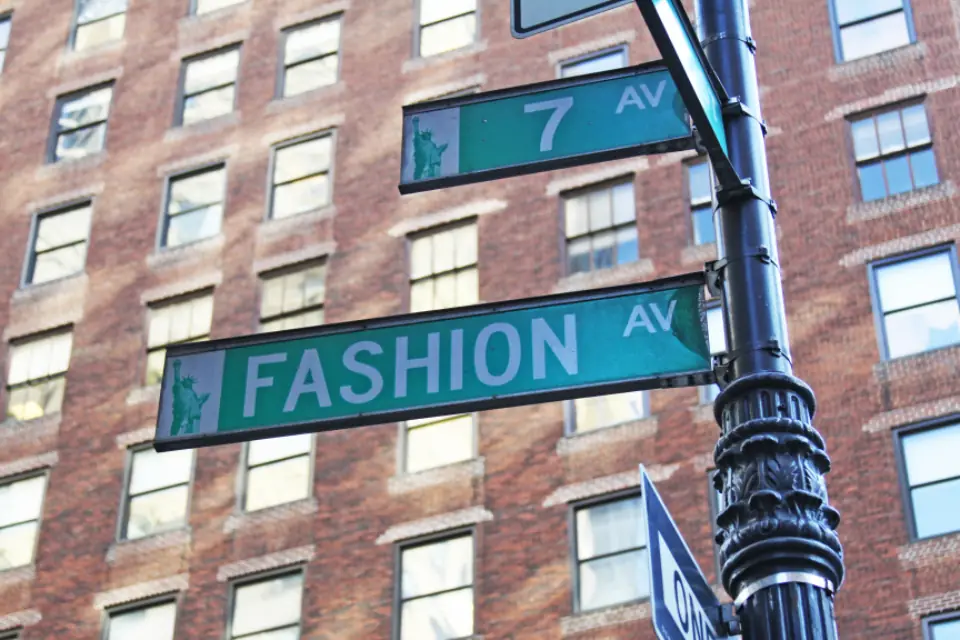 Green street signs on a lamppost in front of a brick building